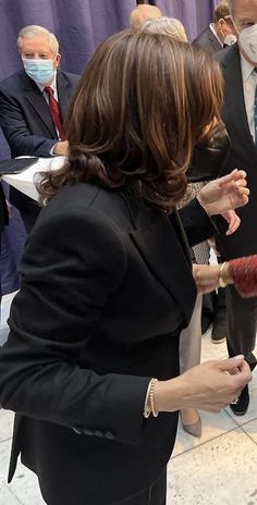 a woman wearing a face mask is talking to people in suits and ties at an event