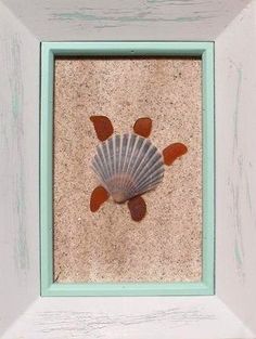 a seashell in a white frame on the sand with sea glass embedded inside it