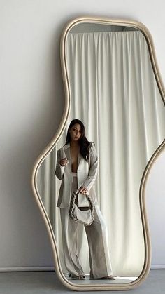 a woman standing in front of a mirror with her hand on her hip and holding a purse