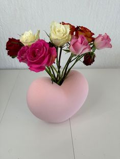 a pink heart shaped vase filled with roses on top of a white table next to a wall