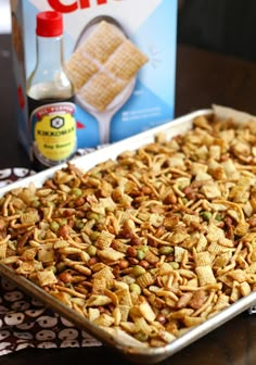 a box of cheetos next to a baking pan filled with crackers and nuts