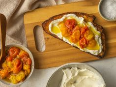 an open face sandwich with tomatoes and cream on a cutting board next to bowls of ice cream