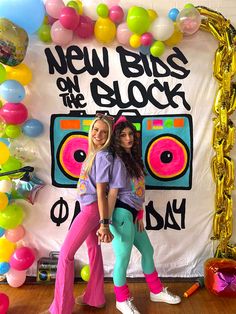 two girls standing in front of a new bliss on the block backdrop with balloons and streamers