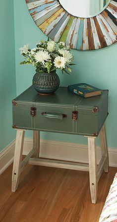 a green suitcase sitting on top of a wooden table in front of a round mirror