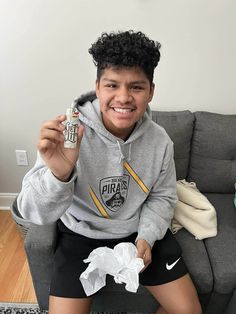 a young boy sitting on a couch holding a cell phone and tissue in his hand