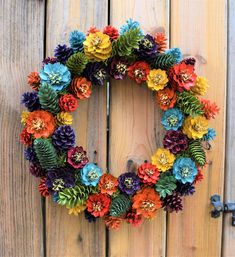 a wreath made out of pine cones and colorful flowers on a wooden fence with an iron hook