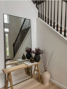 there is a table with vases on it in front of the mirror and stairs