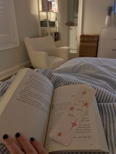 a woman is reading a book on her bed with the pages spread open to show stars