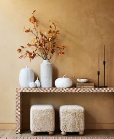 two white vases sitting on top of a wooden shelf next to plants and pumpkins