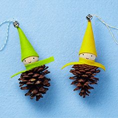 two small pine cones with little gnomes on them hanging from twine strings against a blue background