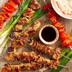 chicken and vegetable skewers with dipping sauce on a wooden table next to rice