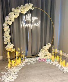 a wedding arch with candles and flowers on the floor next to it that says will you marry me?