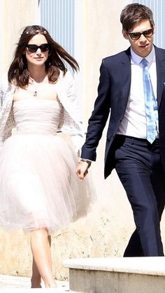 a man and woman dressed in formal wear walking down the street with their hand in each other's pockets