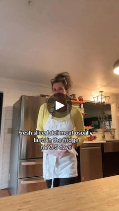 a woman wearing an apron standing in front of a kitchen counter with words on it