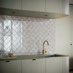 a kitchen with white cabinets and marble tile backsplash, gold faucet