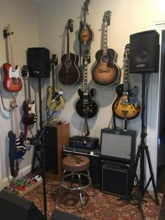 guitars and amps are lined up on the wall in a room with carpeted flooring