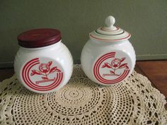 two white jars sitting on top of a doily next to each other with red and white designs