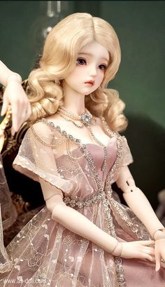 a doll with blonde hair wearing a pink dress and holding her hand out to the side