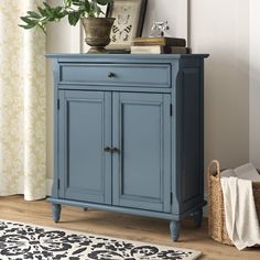 a blue cabinet sitting on top of a wooden floor next to a rug and potted plant