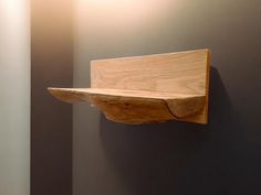 a wooden shelf mounted to the side of a gray wall next to a white light