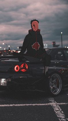 a man sitting on the hood of a black sports car in a parking lot at night