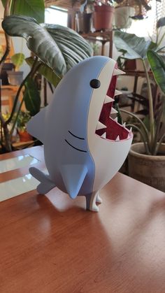 a toy shark with its mouth open on top of a wooden table next to potted plants