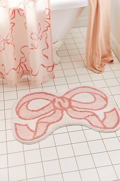 a bath mat with a bow on it next to a toilet in a white bathroom