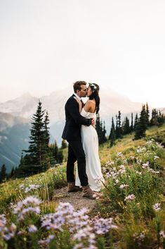 a bride and groom kissing on top of a mountain with wildflowers in the foreground