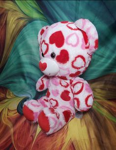 a pink and red teddy bear with hearts on it's face sitting on a colorful background