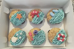 six cupcakes with blue frosting and sea creatures on them in a box