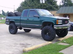 a large green truck parked in a parking lot next to a building with tires on it