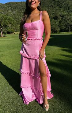 a woman in a pink dress holding a wine glass and posing for the camera on a golf course