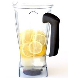 a blender filled with lemons and ice on top of a white table next to a black handle