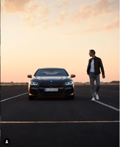 a man standing next to a black car in the middle of an empty parking lot