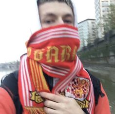 a man wearing a scarf with the word spain printed on it, standing in front of a body of water