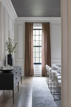 an empty room with chairs and tables in front of a window that has drapes on the windowsill