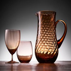 three glasses and a pitcher are sitting on the table next to each other in front of a gray background