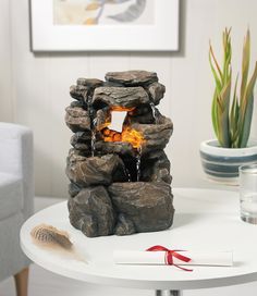 a small fountain made out of rocks with water running down it's sides and red ribbon on the table