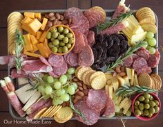 an assortment of meats and cheeses on a platter with olives, crackers, grapes, bread