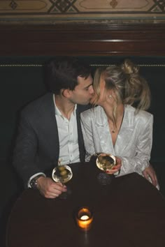 two people sitting at a table kissing each other