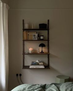 a shelf with books and candles on it in the corner of a room next to a bed