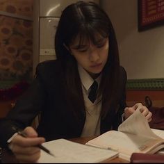 a woman sitting at a table with an open book in front of her and writing