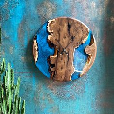 a blue and brown clock sitting on the side of a wall next to a cactus