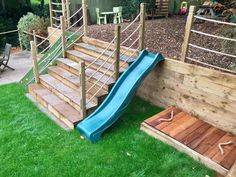 a blue slide sitting on top of green grass next to a wooden deck and fence