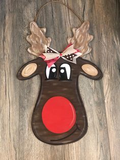 a wooden reindeer ornament hanging on a wood wall with red nose and antlers