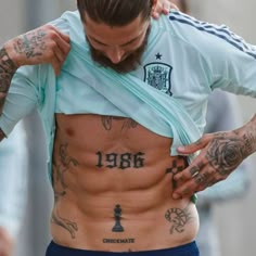 a man with tattoos on his stomach and chest is looking down at the ground while holding onto another mans shirt