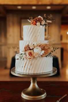 a three tiered cake with flowers on the top is sitting on a table next to a knife and fork