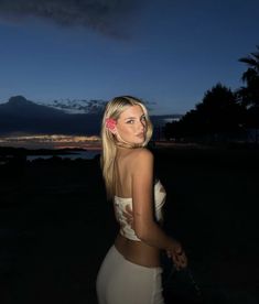 a beautiful young blond woman standing in front of the ocean at night with her back turned to the camera