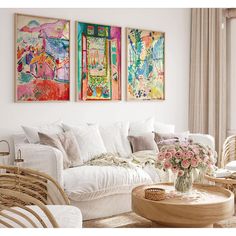 a living room filled with white furniture and paintings on the wall above it's windows