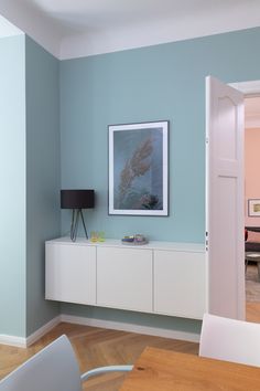 a living room with blue walls and white furniture in the center, along with a painting on the wall